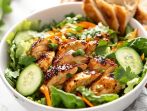 Banh Mi Salad with marinated chicken, pickled veggies, and cilantro in a white bowl drizzled with dressing
