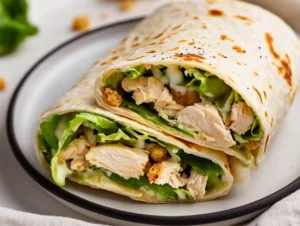 Delicious chicken caesar wrap sliced in half on a white plate, filled with romaine, chicken, and croutons