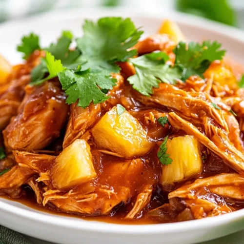 Shredded Crockpot Hawaiian Chicken served on a white plate with fresh cilantro and pineapple chunks